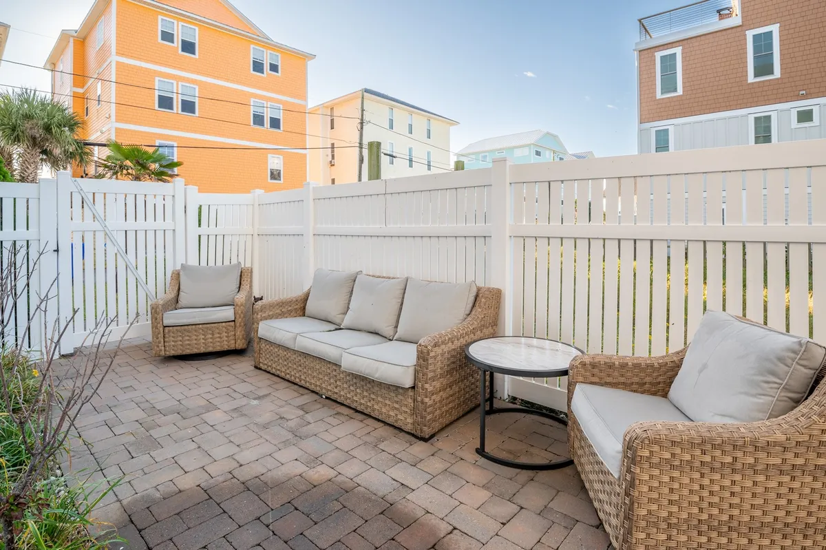 A wicker seating arrangement with a small round table set within a cozy, fenced exterior courtyard, surrounded by colorful houses. The space is perfect for intimate conversations, coffee, or small social gatherings.