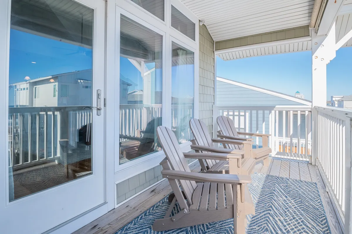 A covered balcony with classic Adirondack chairs and a woven rug overlooks the scenery. The setup is perfect for sipping morning coffee or enjoying sunset cocktails, with a tranquil, inviting atmosphere that brings the ocean breeze into the heart of the home.