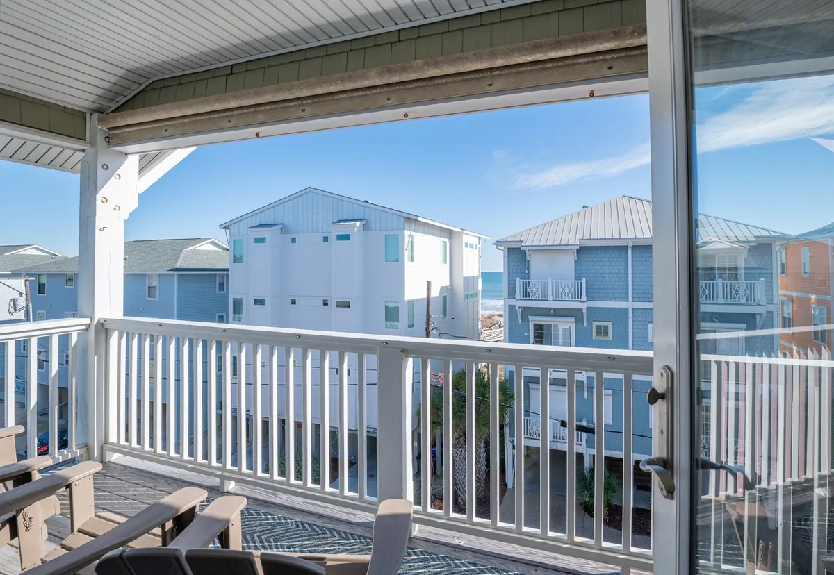 This image features a tranquil balcony space with a railing overlooking the sea and neighboring buildings. The view provides a sense of proximity to water, inviting visitors to relax and enjoy the outdoors. The setting is ideal for morning coffee, evening chats, or simply soaking up the coastal atmosphere.