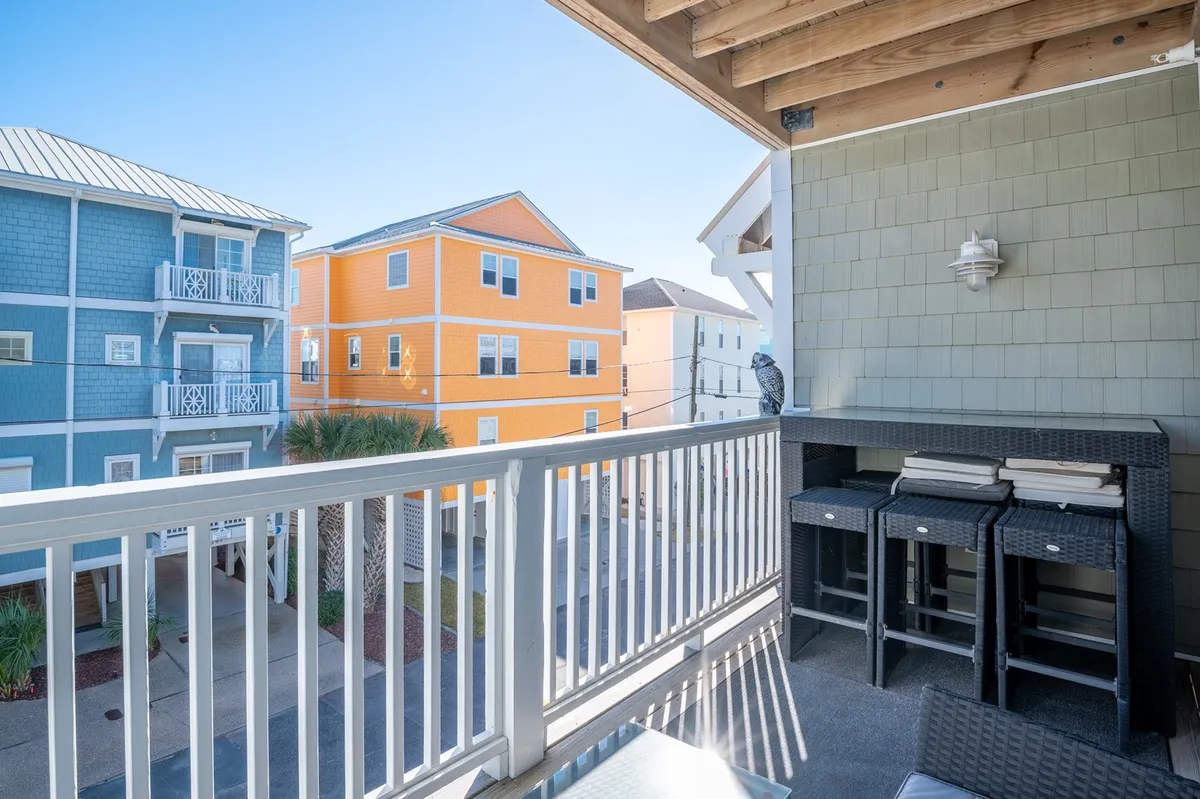 The view captures colorful neighboring buildings from a balcony, accentuated by inviting outdoor seating and decor. The scene is bright, vibrant, and lively, suggesting opportunities for both relaxation and socializing while taking in the local neighborhood.