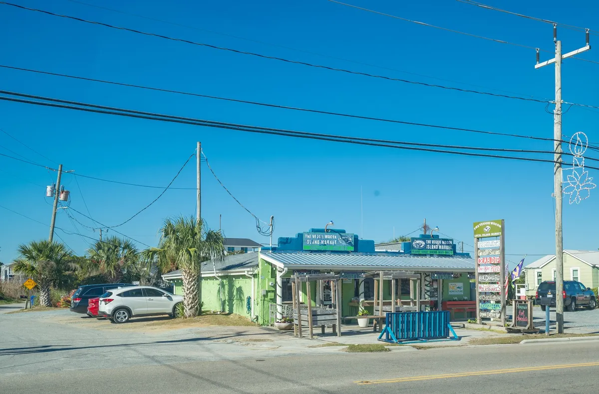 An exterior image featuring a vibrant, colorful building with visible signage and a welcoming parking area. The scene captures diners enjoying outdoor meals while others socialize in a laid-back atmosphere. The patio space suggests a lively environment ideal for gatherings or casual nights out, and the setting sun hints at an inviting nightlife scene.
