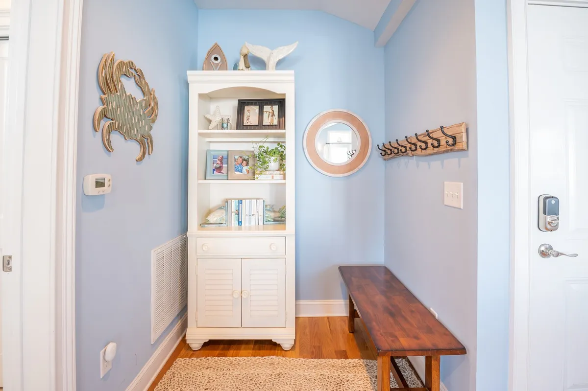 An entry area featuring a shelving unit, mirror, wooden bench, coat hooks, and coastal decor. It captures the feeling of arrival, with space for guests to hang coats and store shoes, setting a communal and welcoming tone.