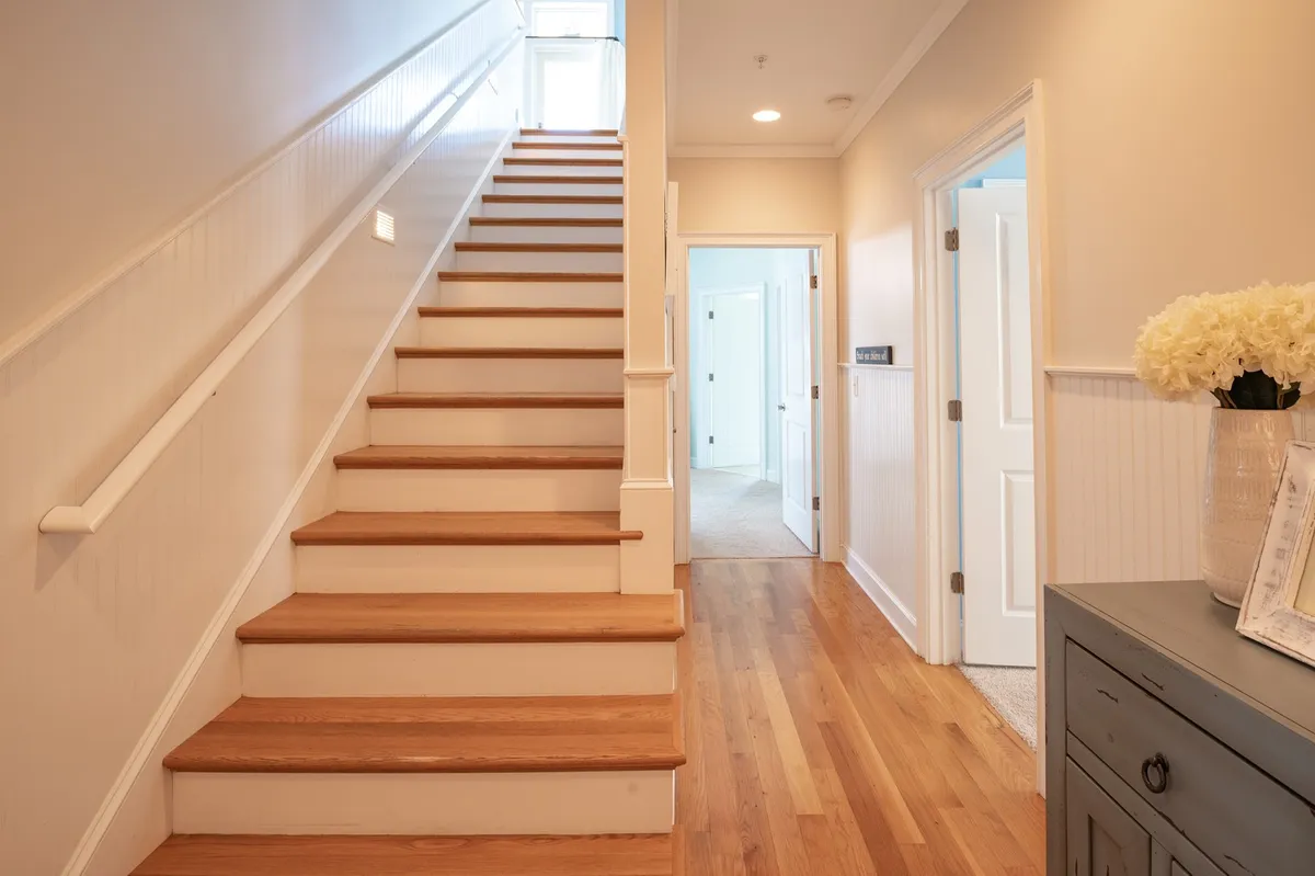 A bright hallway with stairs and a decorative vase, suggesting a spacious and open transition area perfect for larger groups to move between floors. The doorway hints at access to multiple areas, supporting the theme of connected yet private spaces.