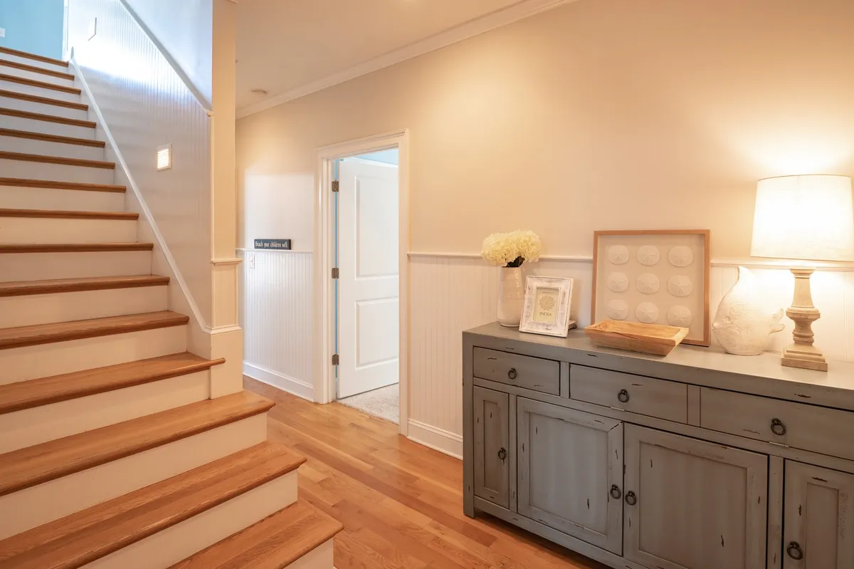 A warm and inviting entryway featuring a staircase, console table with a lamp, and decorative objects. The space is filled with light and offers a welcoming atmosphere, perfect for first impressions and group arrivals.