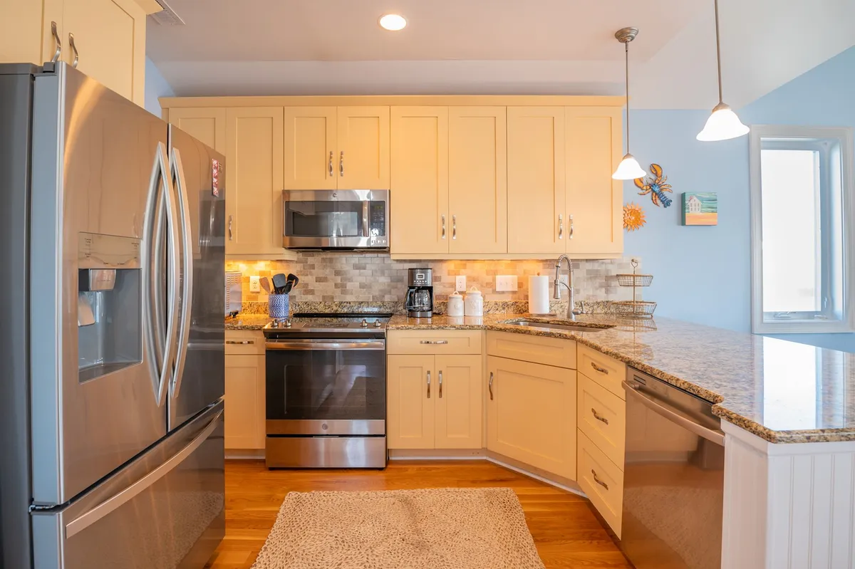 A close-up of the chef’s kitchen, highlighting upgraded stainless steel appliances, granite countertops, pendant lighting, and a welcoming kitchen island. The space is bright and inviting, perfect for collaborative cooking and casual breakfasts.