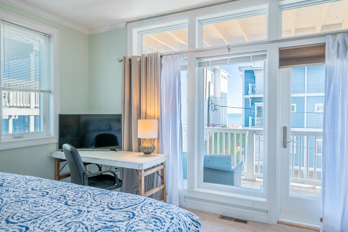 A tranquil king suite featuring a bed with blue patterned bedding, a desk with a computer for remote work, and large glass doors leading to a private balcony. Soft lighting and serene decor create a restful ambiance, while the balcony hints at ocean views and a private space for relaxation.